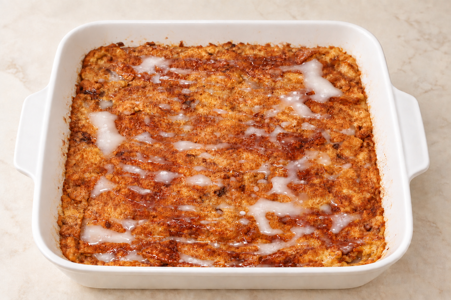 Vegan gluten-free cinnamon-raisin baked French toast with glaze in a white baking dish for your Vegan Yom Kippur Break Fast.